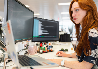 Woman looking at computer screens sitting at desk.